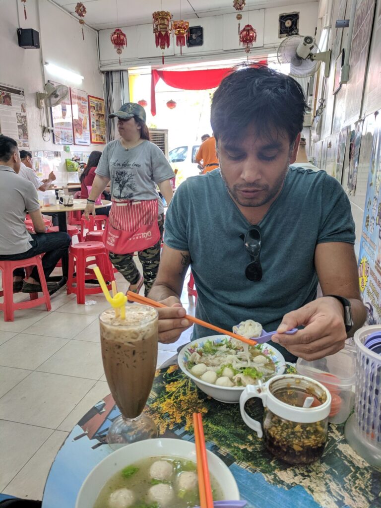A man in a restaurant eating a bowl of meatballs and noodles