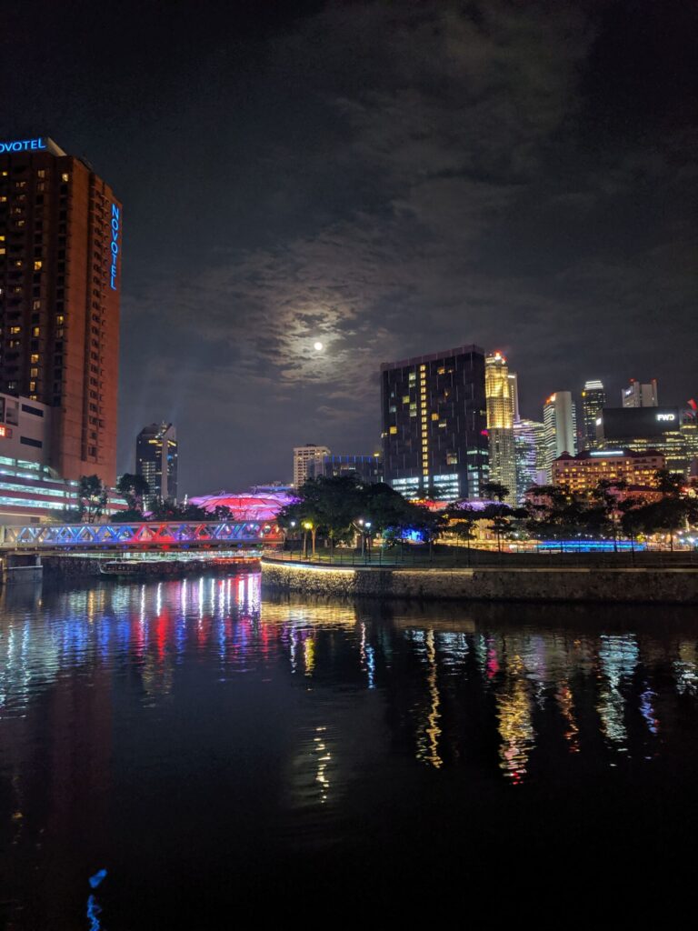 The Singapore city skyline at night with a moon masked by clouds