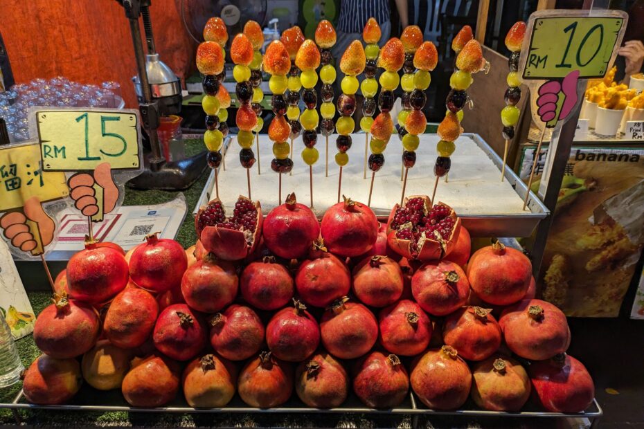 A fruit stall at a night market with pomegranates stacked on top of each other and fruit sticks behind