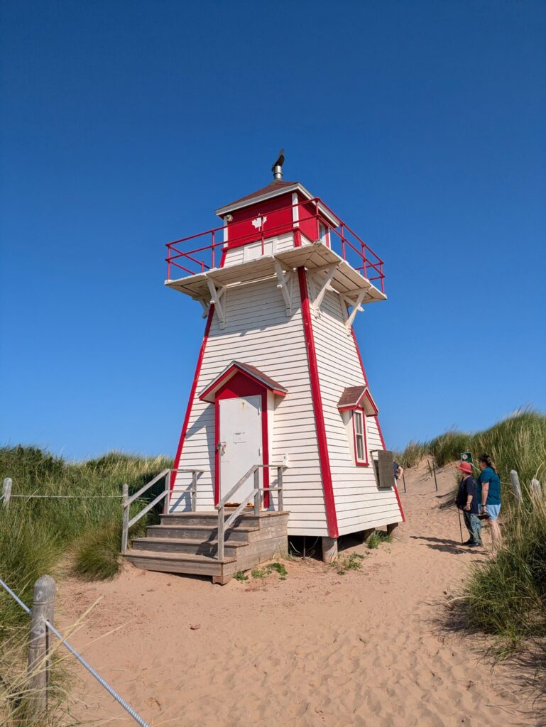 A wooden lighthouse on a beach with 2 people looking at it