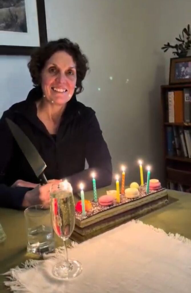 A woman smiling at the camera with birthday cake with candles in front of her