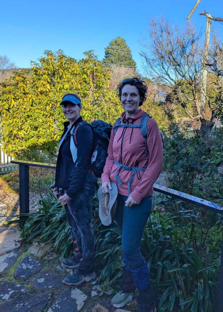 Two friends on the front steps of a house, smiling at the camera, about to leave for a hike