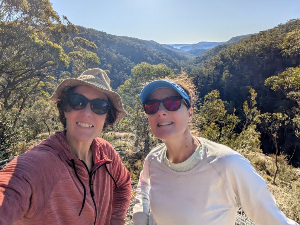 Two women at a lookout with mountains and bush in the background