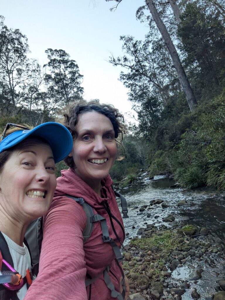 Two women smiling at the camera in the bush, pretending everything is ok