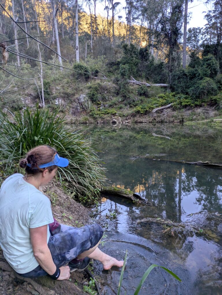 A woman cleaning her feet in a cold river in a bush setting