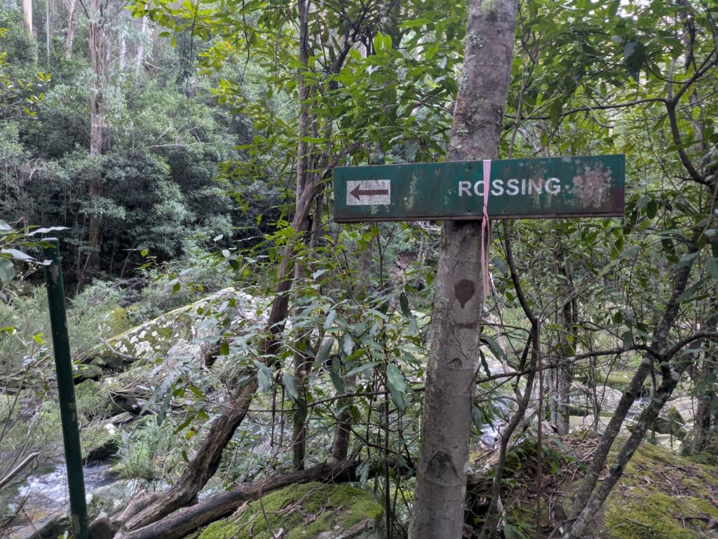 A dirty sign with letters missing, pointing the wrong way on a path
