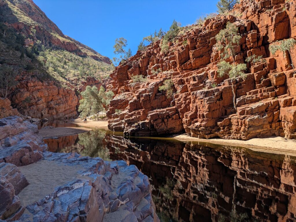 A gorge with red rocky cliffs and a still pool of water at the base