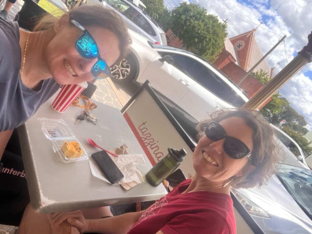 Two friends sitting at an outdoor table of a bakery eating lunch