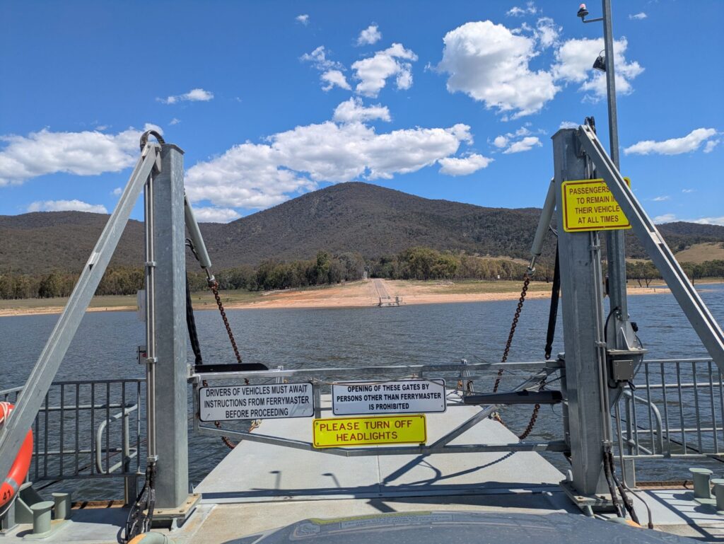 Looking from a vehicle out to the safety signs and structures that make up a car ferry with the destination of the ferry in the distance