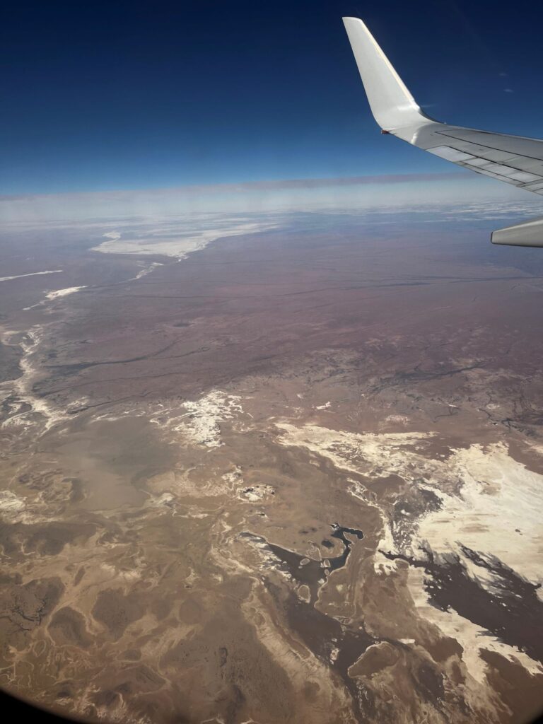 A view out of a plane window over lake tributaries with evidence of salt white patches