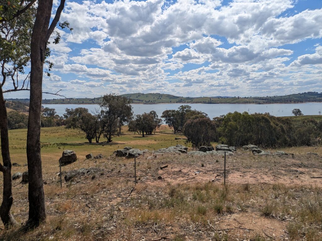 Looking towards a large river with rolling hills of farm land on both sides and some rocks in the foreground
