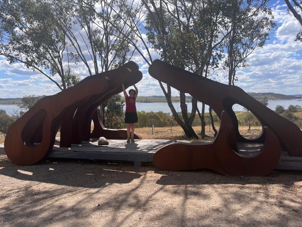 A woman standing with her arms above her head to reach the top inside of a sculpture of two hands