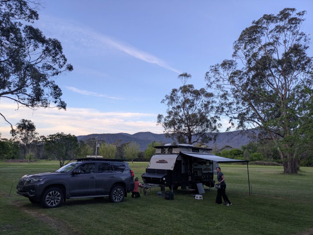 A large car pulling a caravan, parked in a lush camp ground