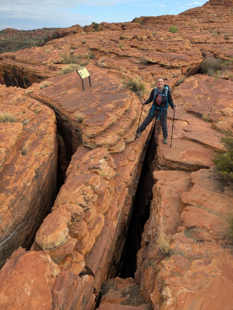 A woman standing with one leg on either side of a giant crack in a rock formation