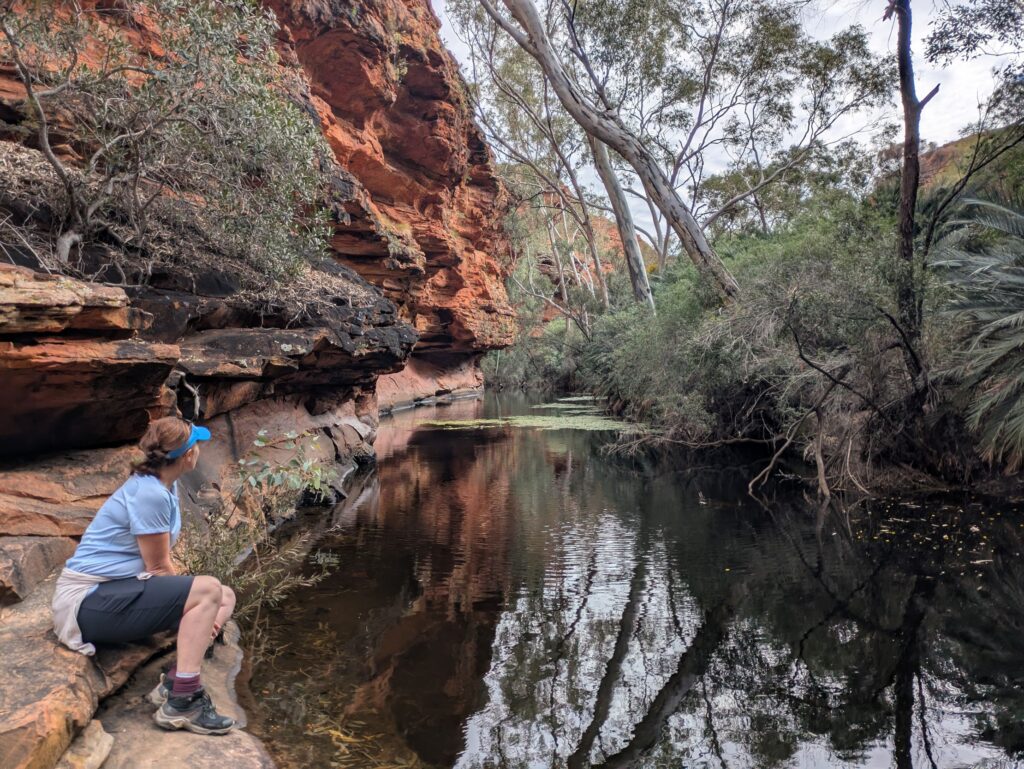 A woman looking away from the camera while she sits by a water body at the base of a canyon