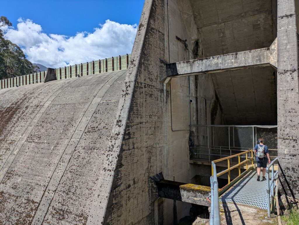 A woman walking along a secure walkway to enter into a large concrete dam wall