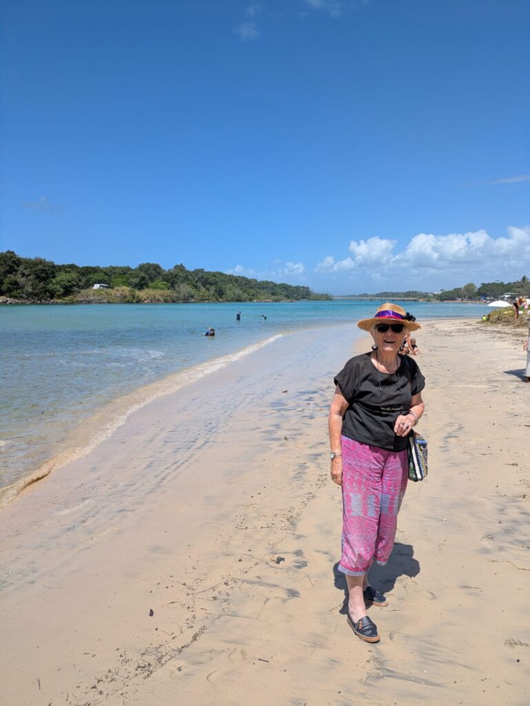 a woman on the sandy banks of a river with people swimming in the background