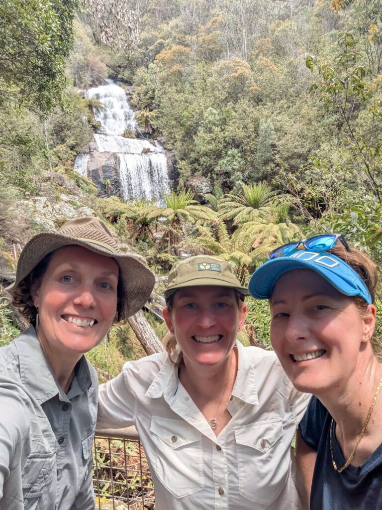 Three friends posing in front of a waterfall in the Australian bush