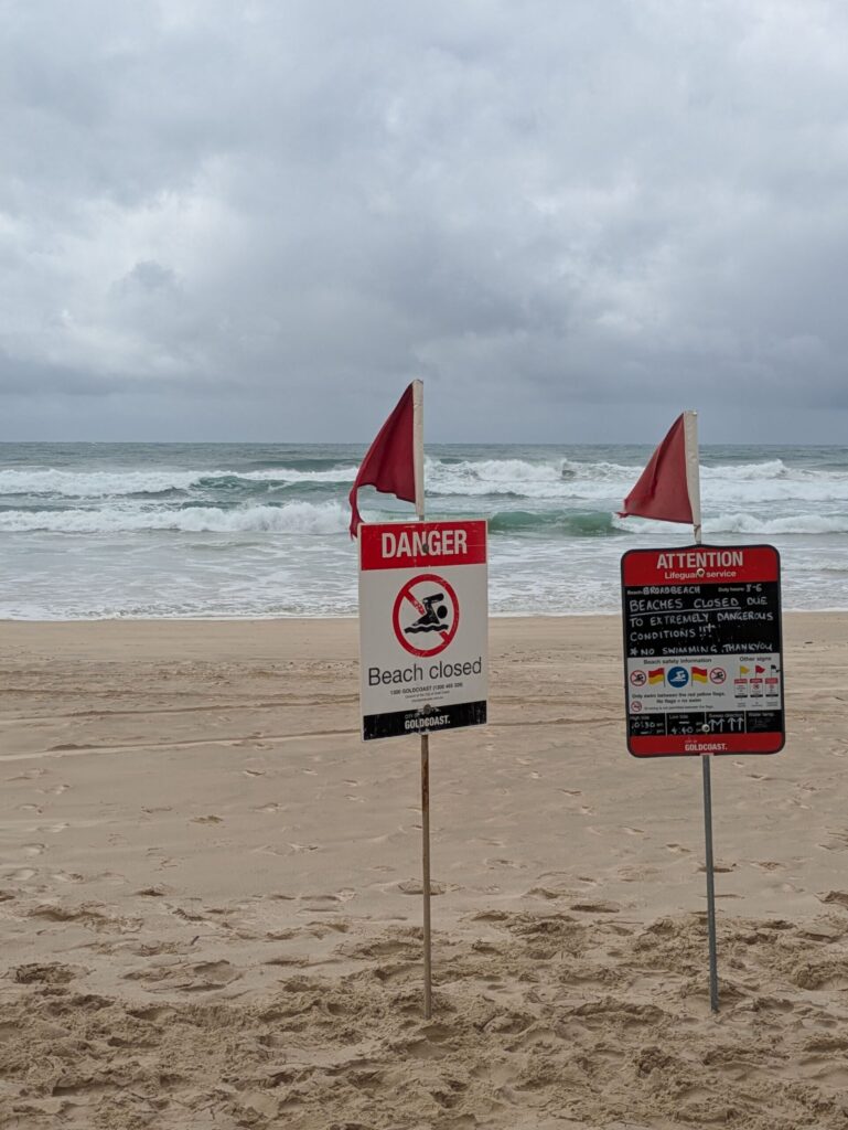 Two signs on a beach indicating the Beach is closed due to a cyclone