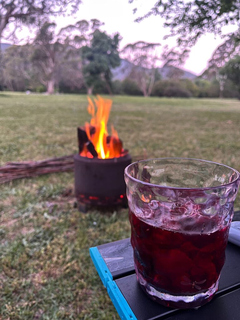 A small camp fire in the background and a berry cocktail in the foreground