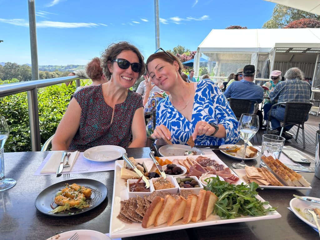 Two friends enjoying a large cheese and meat platter at an outside table at a winery