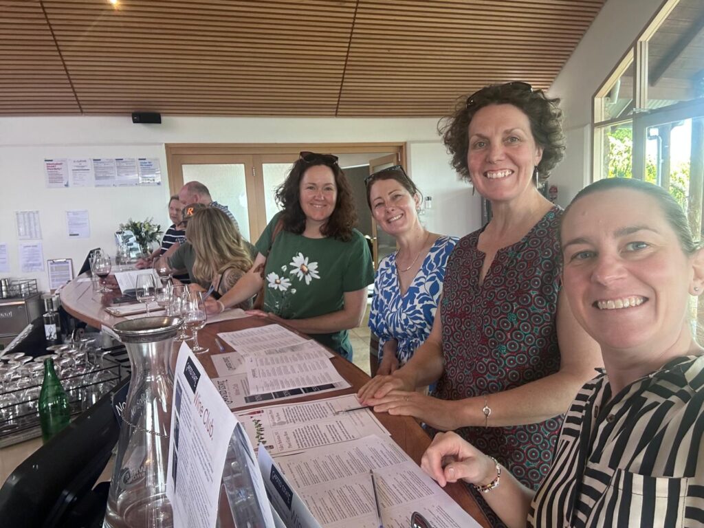 Four friends standing at a bar with papers and empty wine glasses ready to try some wine at a winery