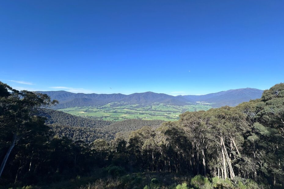 A view from a high lookout over a green valley with mountains in the distance and blue sky around