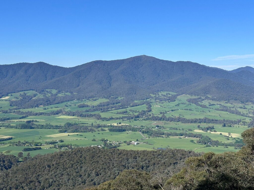 A view from a lookout over a green valley with mountains in the distance