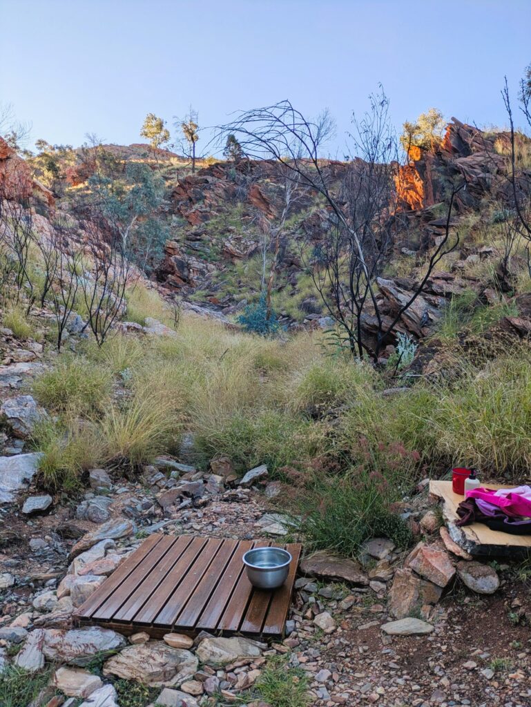 A wooden platform next to a rock ledge in a small canyon which is used as a shower