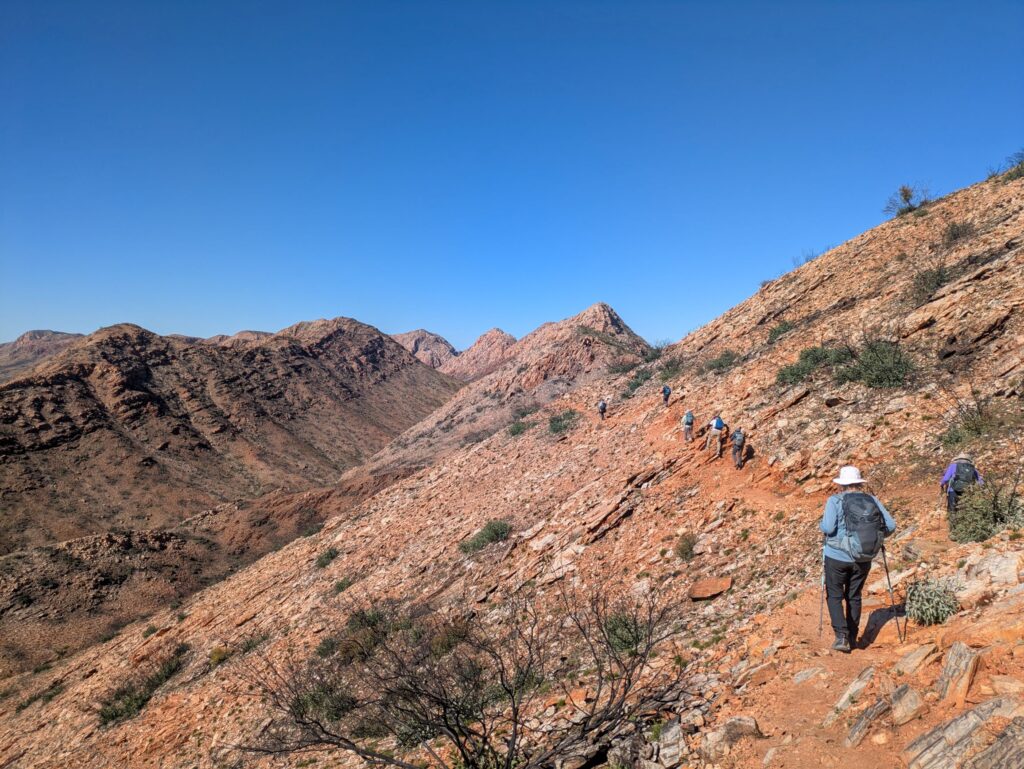 A footpath carved into the side of a steep bare rocky mountain being followed carefully by a group of hikers