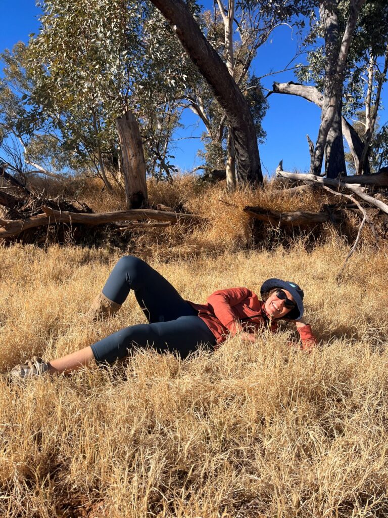 A woman laying on her side in long buffalo grass, smiling at the camera