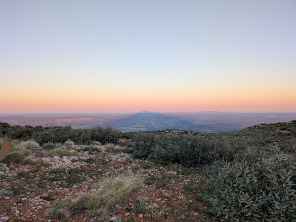 Looking from a high point, a shadow of a mountain reaching across the landscape and appearing to reach above the horizon