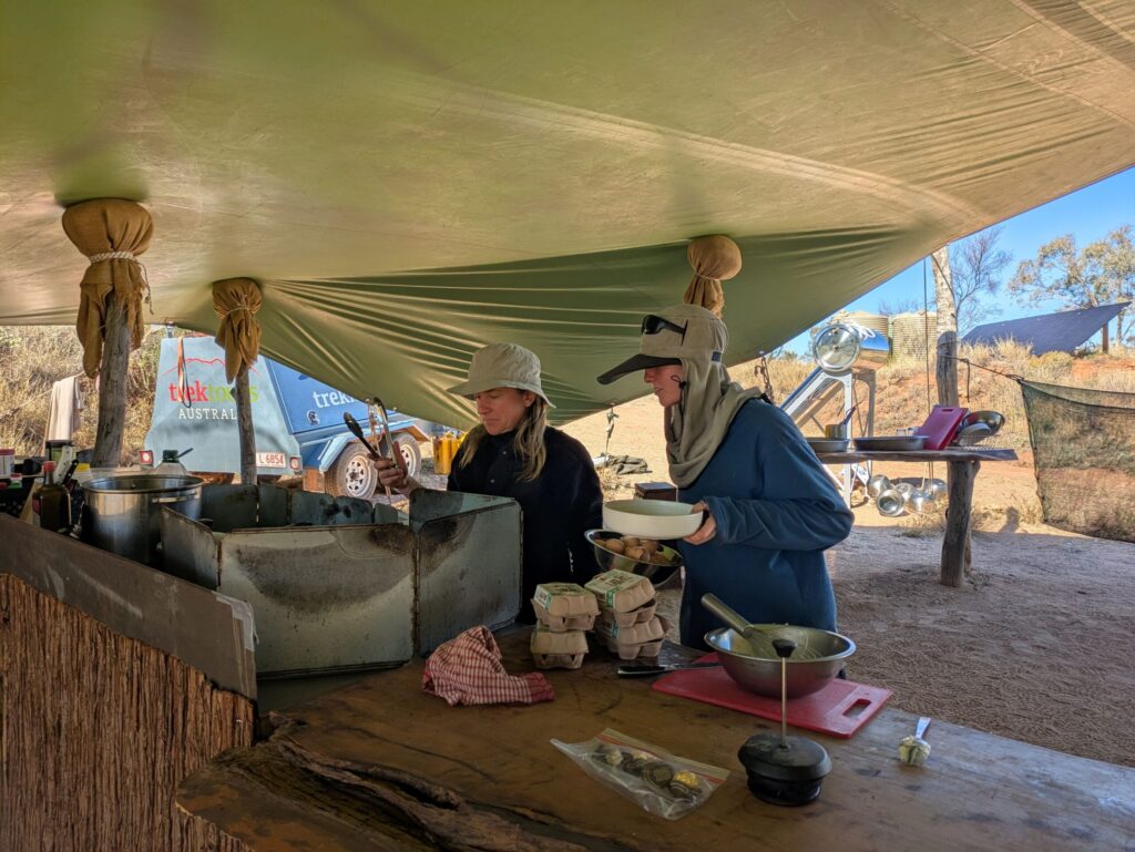 Two women cooking a few dozen eggs at the camp kitchen stove
