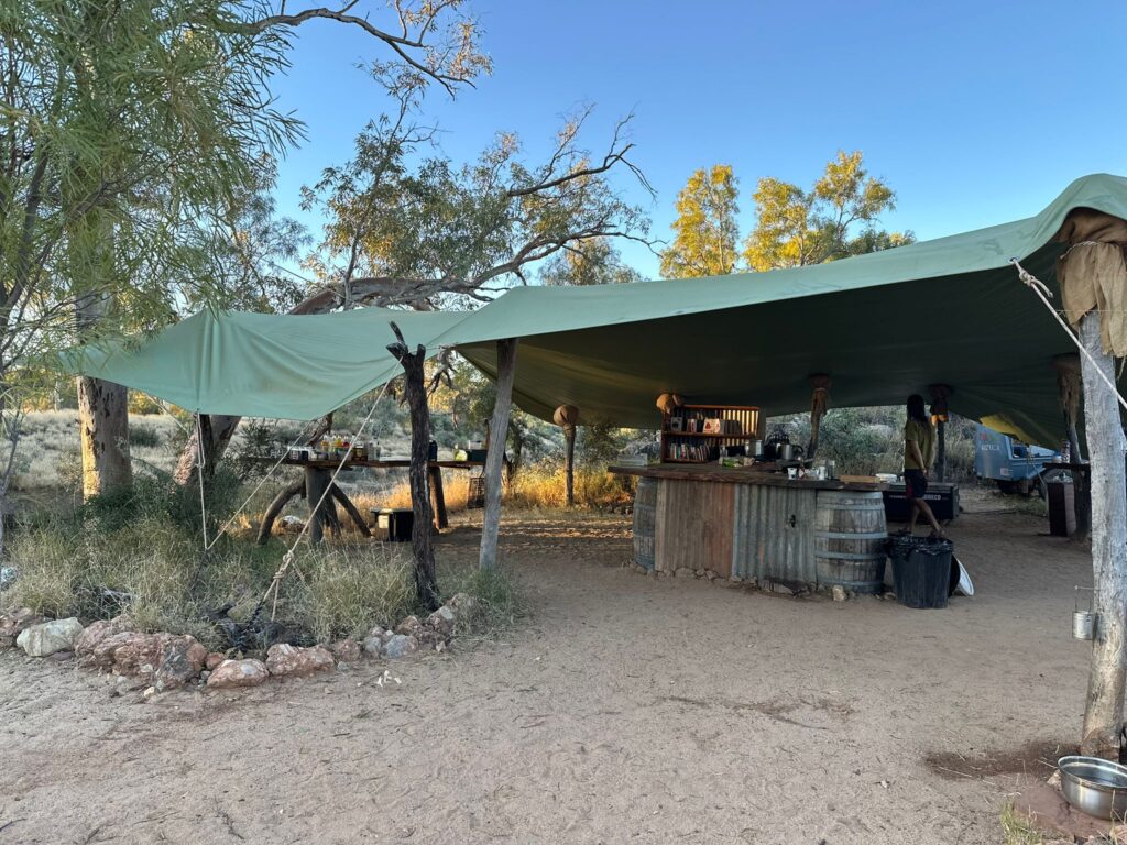 An outdoor kitchen protected by 2 large tarpaulins held up by tree trunks