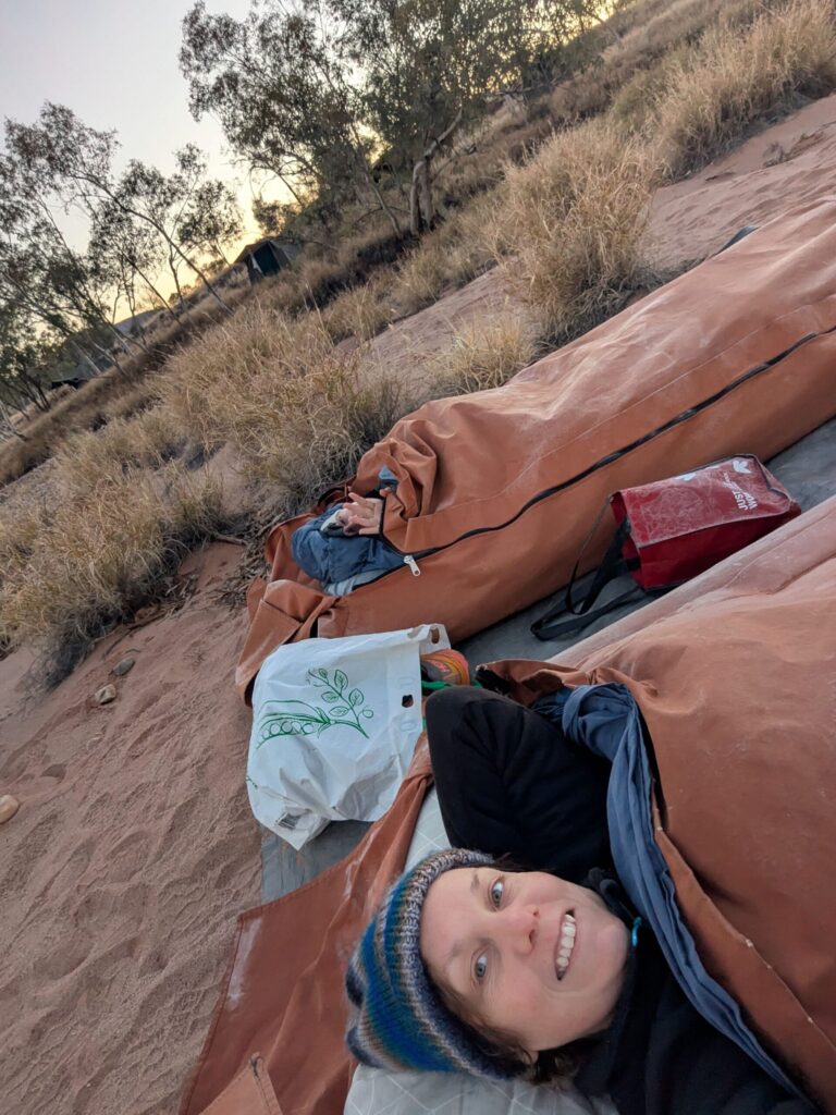 two women sleeping in separate swags in a dry river bed with frost on their belongings