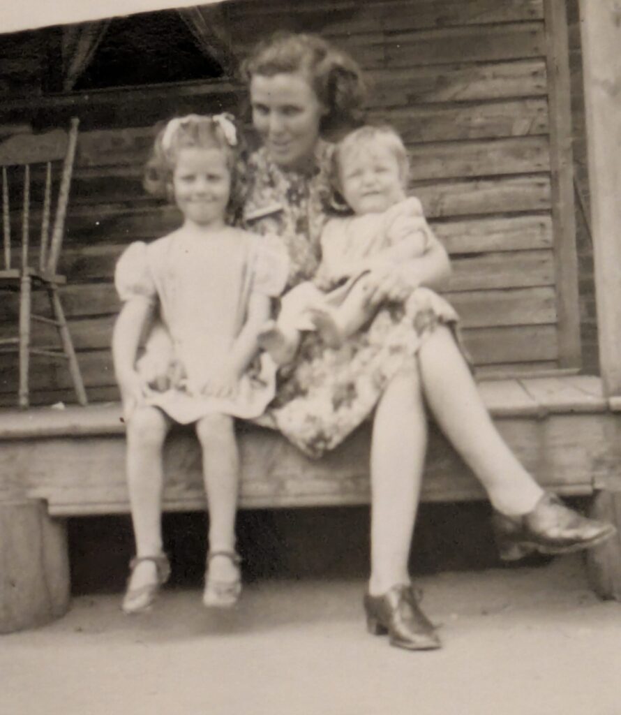 A black and white photo  from 1947 of a mother sitting on a porch with her two young daughters