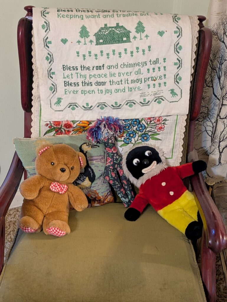 A small teddy bear and a gollywog doll propped up on a older style wooden chair