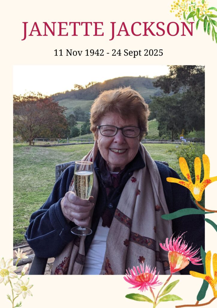 A woman sitting outside in a rural setting with a glass of bubbles in her hand and a big grin on her face 
