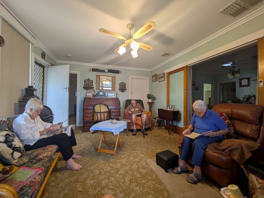 In an older style loungeroom, three people sitting separately across the room reading different materials on their laps