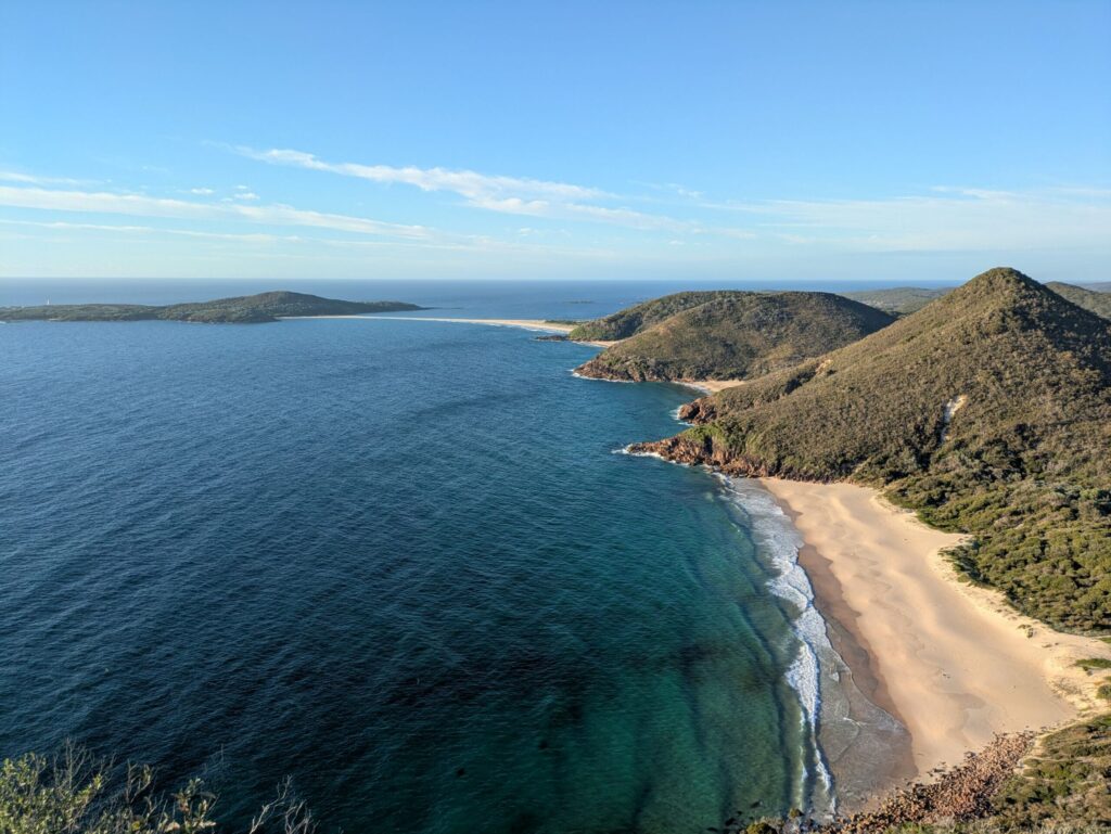 A series of white sandy beaches and small green mountains along the coast line with the ocean