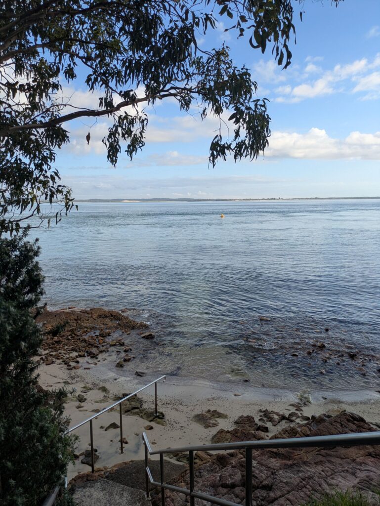 Standing at the top of some steps, looking down to a rocky beach and a calm ocean