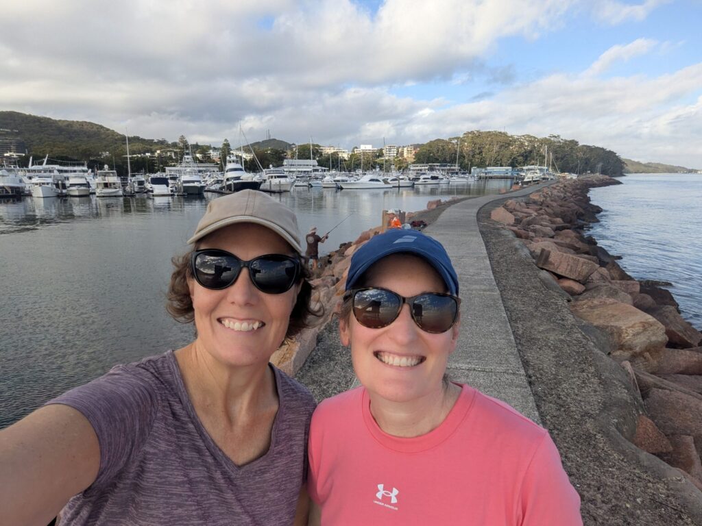 Two friends looking at the camera with a breakwall around a marina full of boats in the background