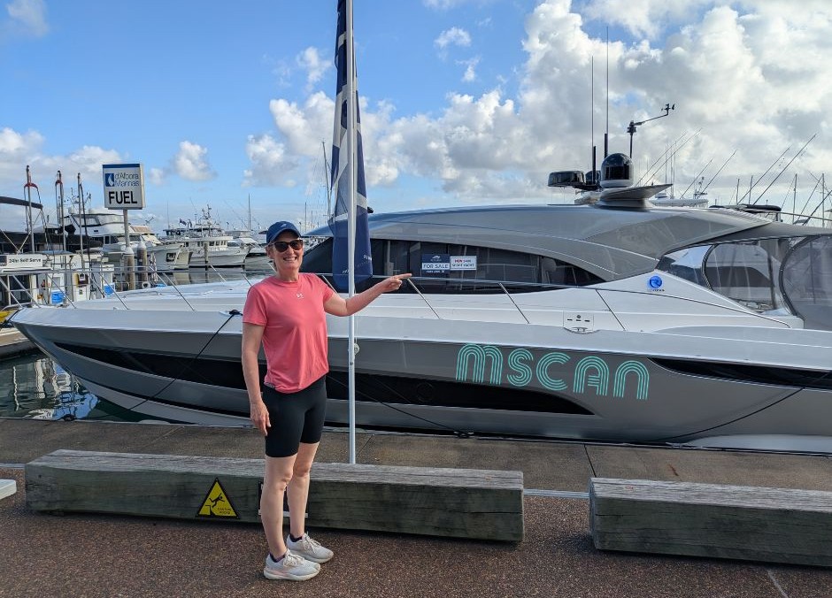 A woman pointing to a For Sale sign on a yacht, intimating that she could buy the yacht