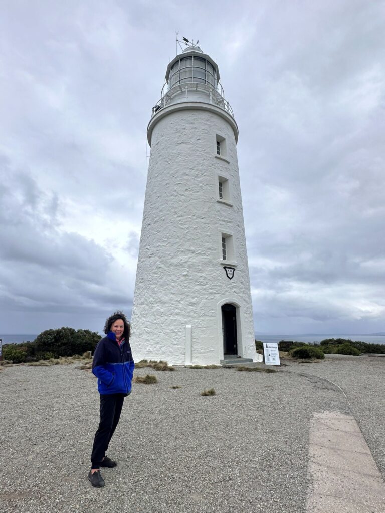 A woman standing in front of an old white lighthouse on a cold, blustery day