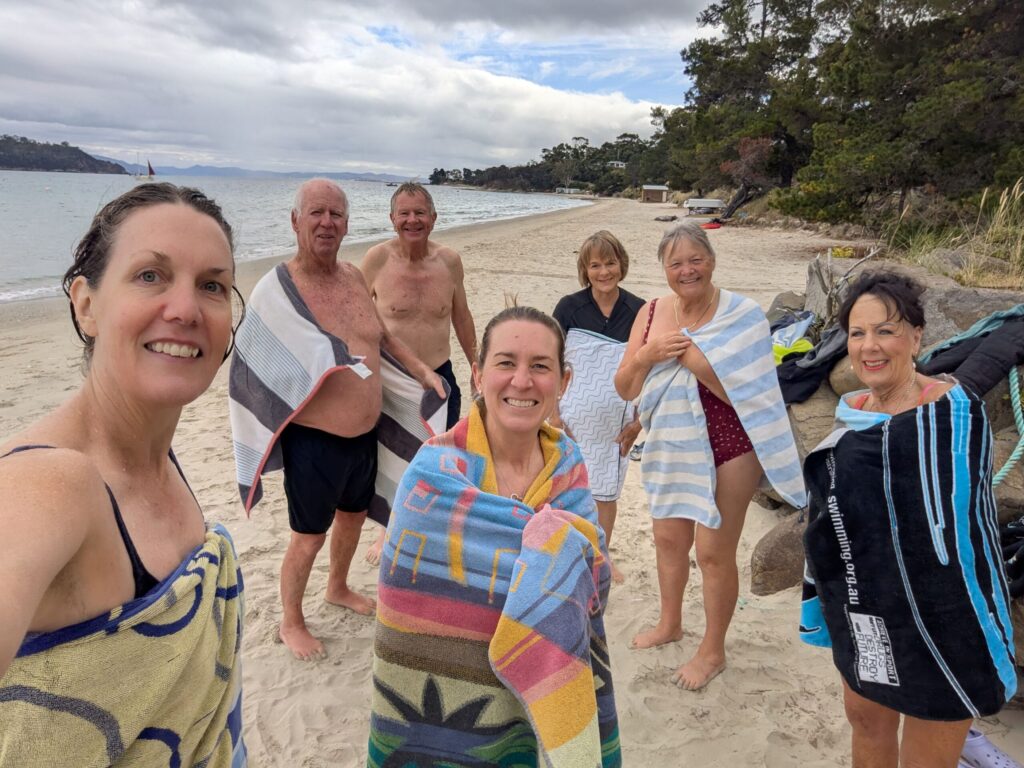 A group of friends wrapped in towels standing on a beach after a very cold morning swim in the ocean