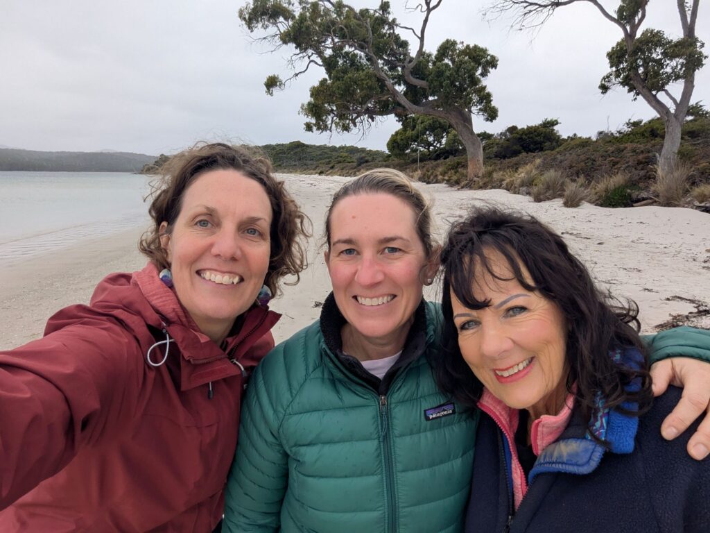 A selfie of 3 friends on a white sandy beach on a cold day