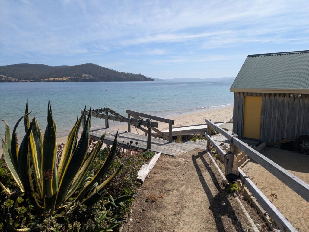 A view from the path of a boathouse and boatramp leading into the ocean on a nice bright day