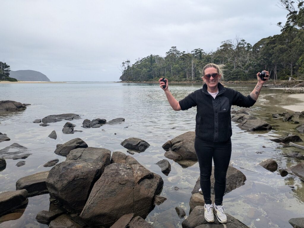 A woman holding freshly foraged mussels in her hands standing on a rock in a lagoon
