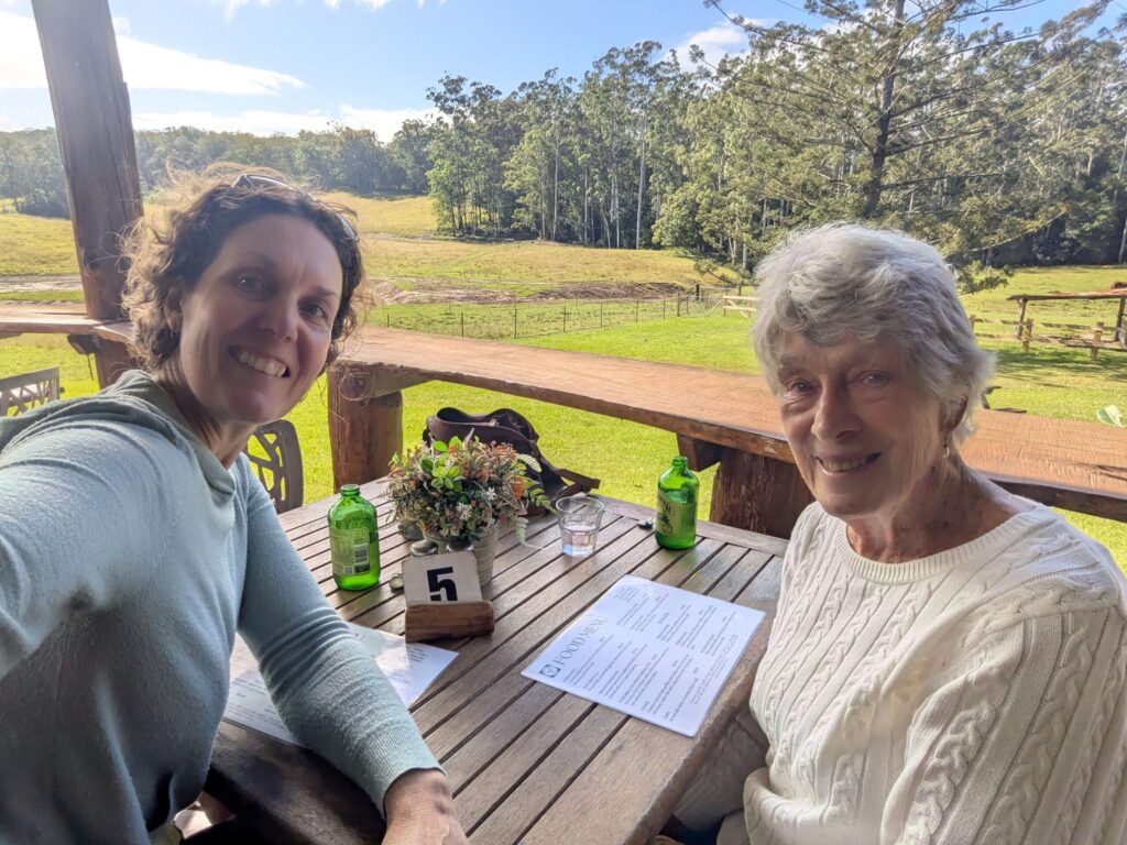 Two women seated at a table on an outdoor of a restaurant with a farm setting behind them