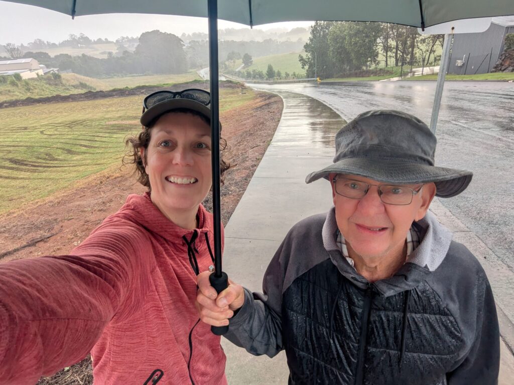 Two friends walking on a footpath through a hilly landscape in the rain with an umbrella